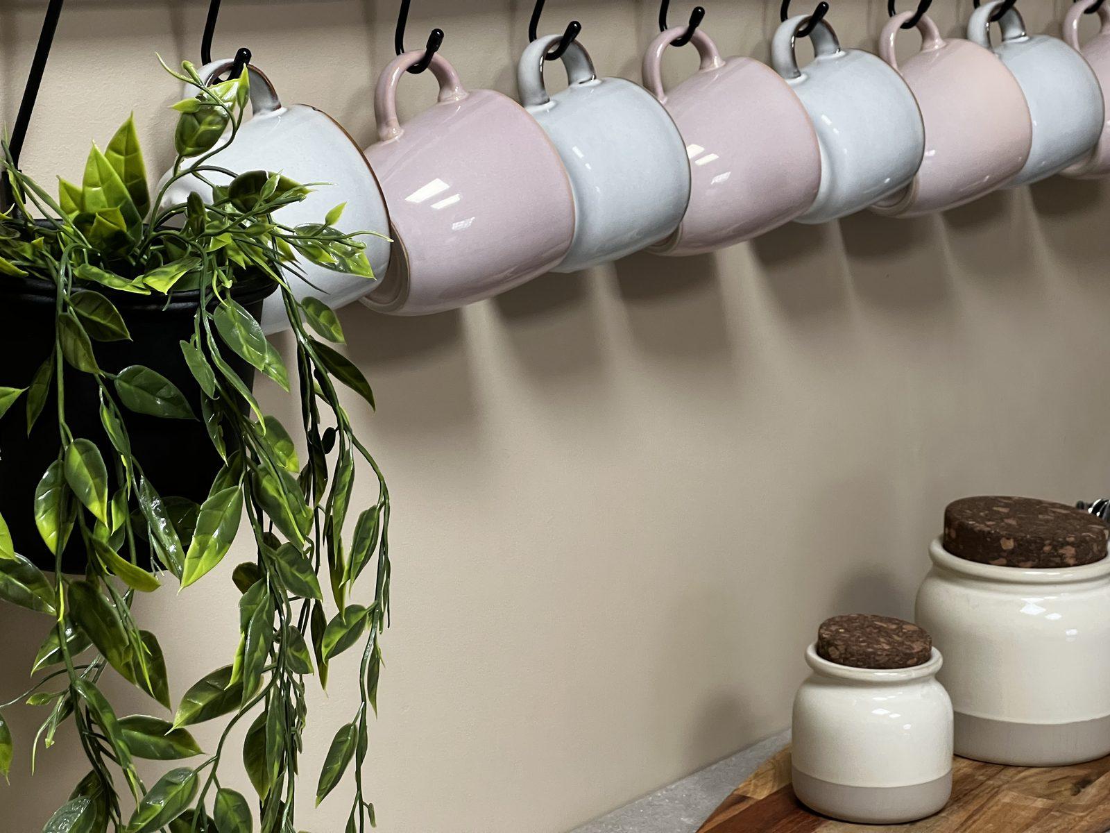 Pink and grey mugs hanging on hooks above storage jars in the kitchen