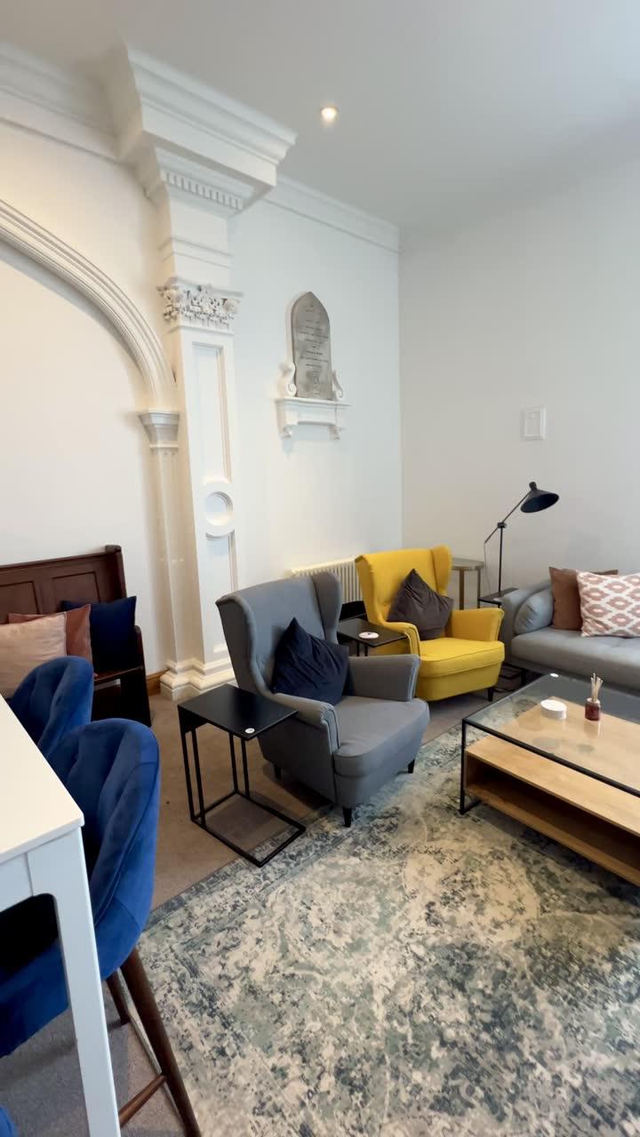 Sofas and a yellow armchair around a low wooden table, beside a stone archway