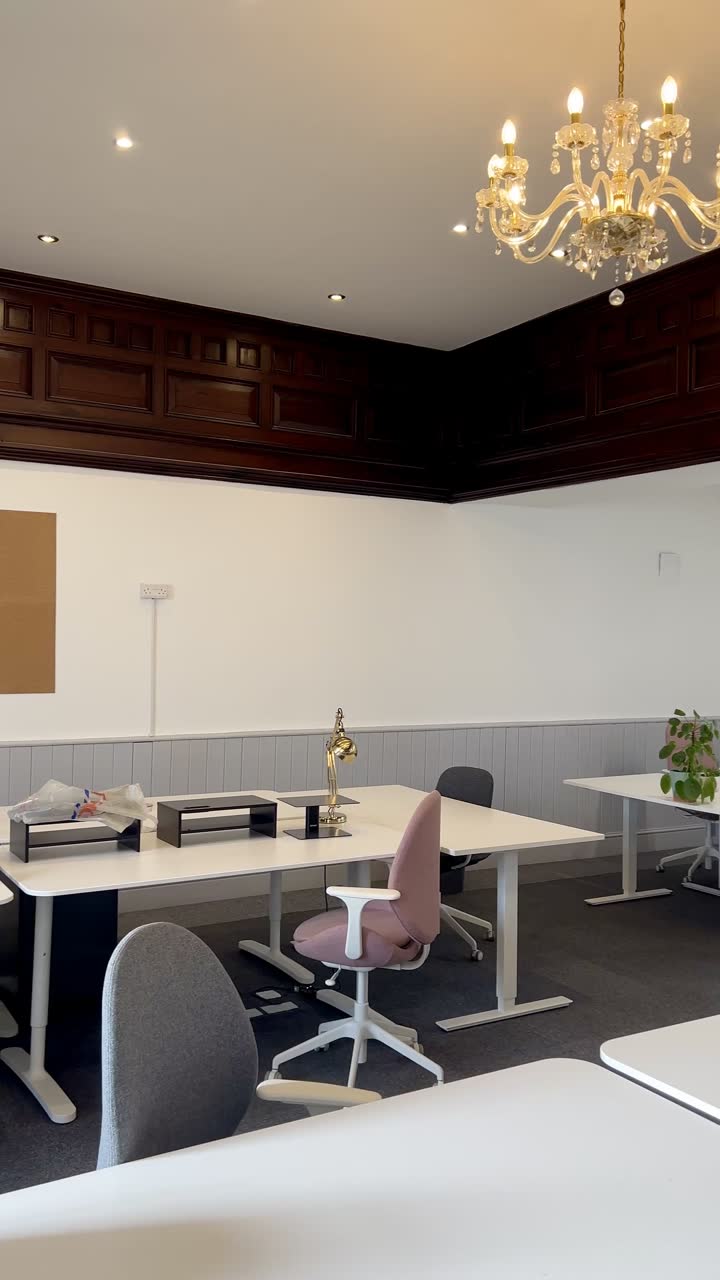 White sit-stand desks and chairs under a cut-glass chandelier, with dark panelling above the picture rail