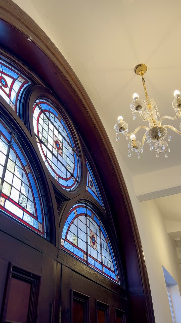 The arched stained-glass window above the chapel doors, lit blue and red, beside a cut-glass chandelier