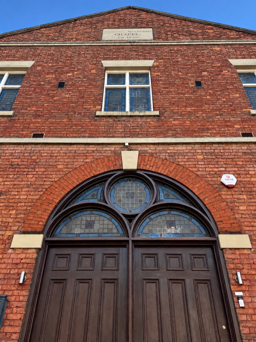 The red-brick front of The Chapel on Welsh Row, with an arched stained-glass window above its wooden doors